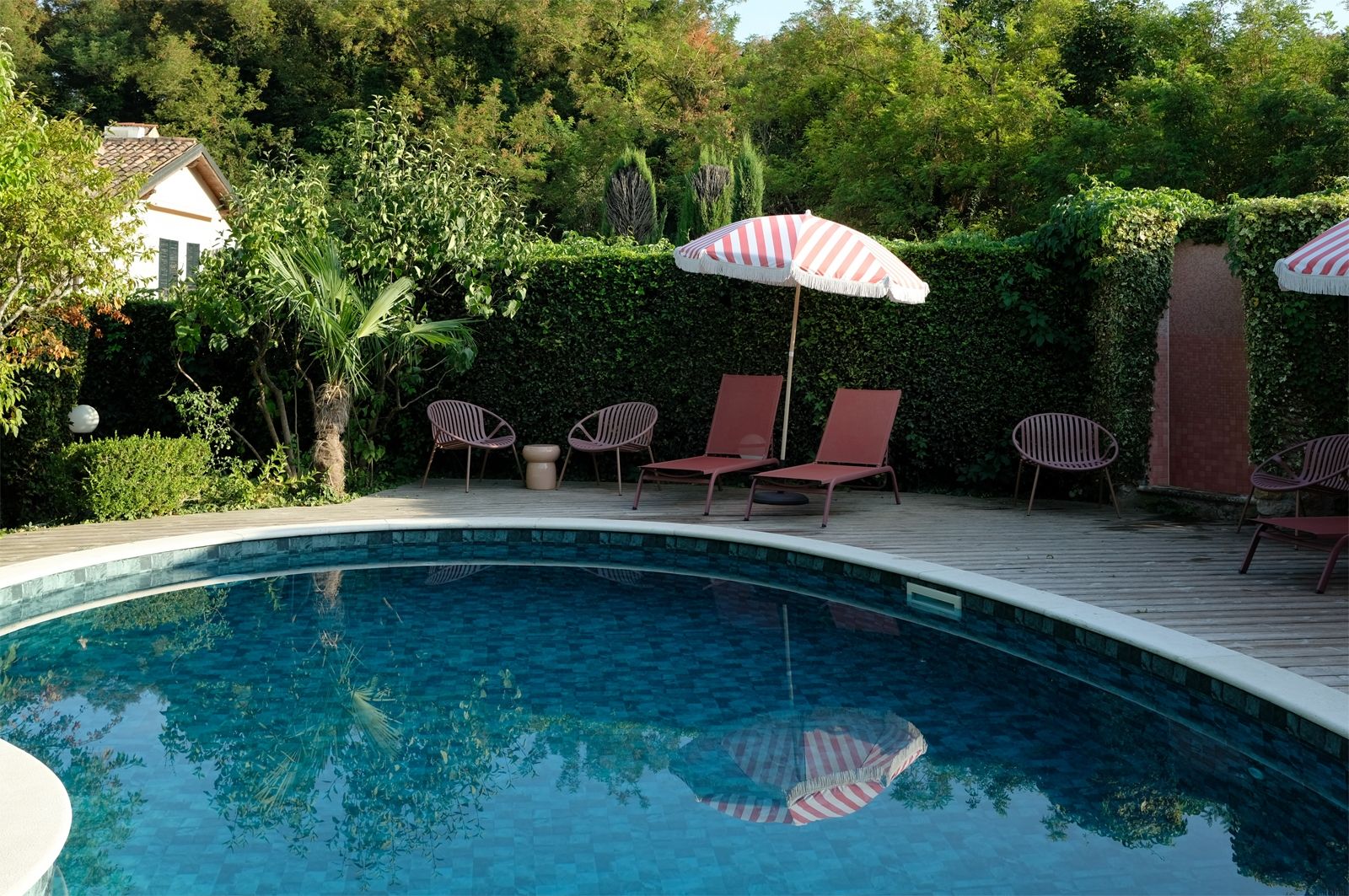 Retro Feeling – Die ursprüngliche Nierenform des Pools (aus den 1970er-Jahren) wurde bei der Sanierung des Anwesens erhalten; Fransenschirme und Outdoormöbel in rosaroten Farbtönen machen den Urlaubsvibe perfekt 