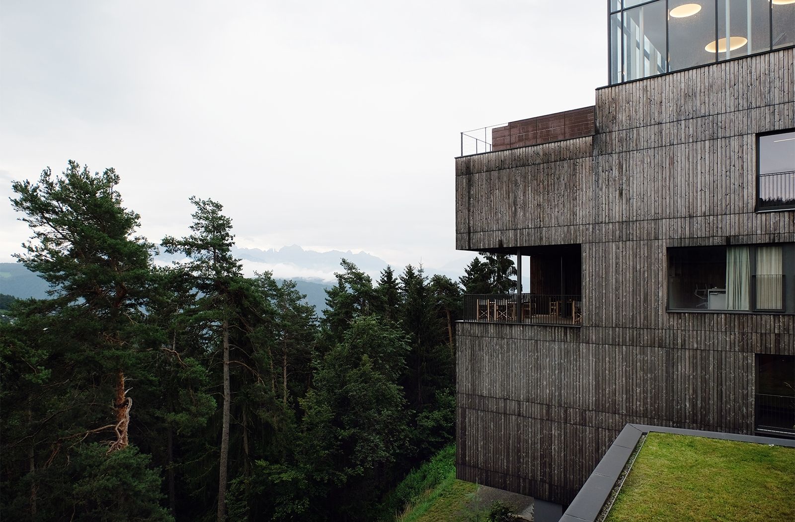Wald, Weite und Berge umgeben das Eco Hotel und lassen die Gäste (nicht nur im verglasten Rooftop) zur Ruhe kommen; Das Holz der Fassaden stammt zum Teil von den Bäumen, die für den Bau der zwei neuen Gebäude, gefällt werden mussten, der Porphyr des Aushubs wurde zu Bodenfliesen 